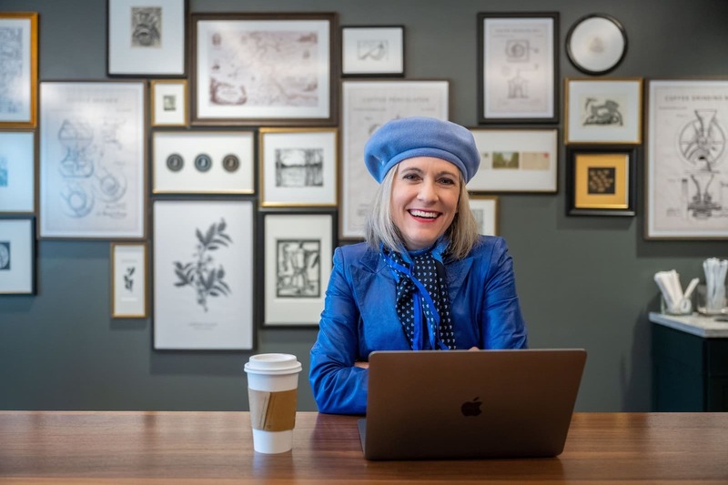 Alison Rice sitting behind a laptop and wearing a blue outfit and hat.
